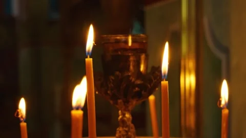 Close-up of several lit candles burning in a dimly lit church interior, with a Stock Footage 346672105