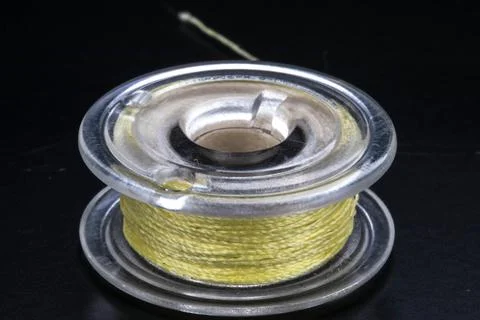 Close up of a sewing machine bobbin with yellow thread on a black background. Foto stock