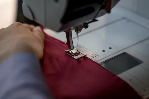 Close-up of sewing machine stitching red fabric with hand guiding material Stock Photos