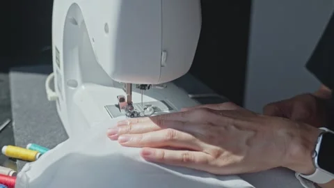 Close up of sewing machine stitching white fabric with hand guiding Stock Footage 314644340