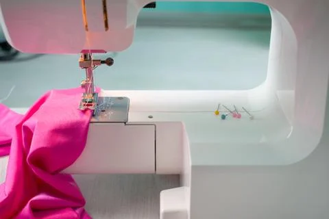 Close up of sewing machine working with pink fabric and pins on a table. Home Stock Photos