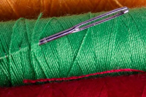 Close-up of sewing needle on green thread spool with red background. Stock Photos
