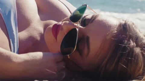 Close up of a sexy girl lying on the beach in sunglasses with big tits Stock Footage