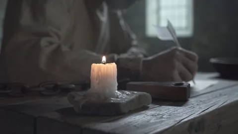 Close up of shackled prisoner hands pinching a candle flame inside a gloomy cell 스톡 동영상 339631391