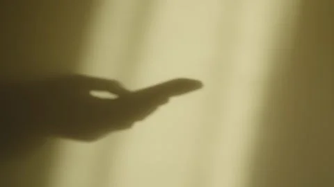 Close up of shadow on a wall of hands holding using smartphone mobile typing Stock Footage 345278164