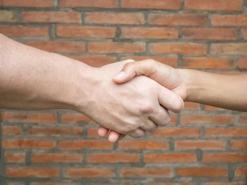 Close-up of shaking hands between man and woman with brick background Stock Photos
