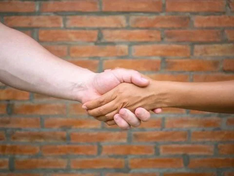 Close-up of shaking hands between man and woman with brick background Stock Photos