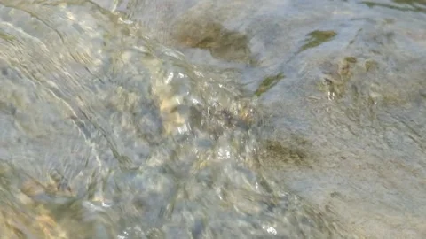 Close-up of a shallow and clear river current flowing over a visible riverbed Stock Footage 336878313