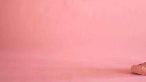 Close up of shapely female legs walking in sneakers on coral background Stock Footage 104057043