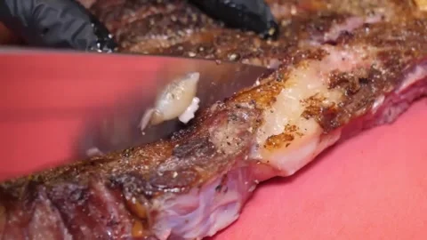 Close-up of a sharp knife slicing into delicious, cooked pork ribs on a red cutt Stock-Footage 332815195
