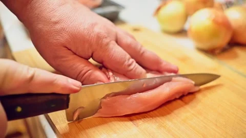Close-up of sharp knife smoothly slicing chicken breast on wooden cutting boa Stock Footage 311753396