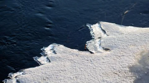 Close-up of a sharp, snow-covered ice edge melting along the dark, ripples .. Stock Photos