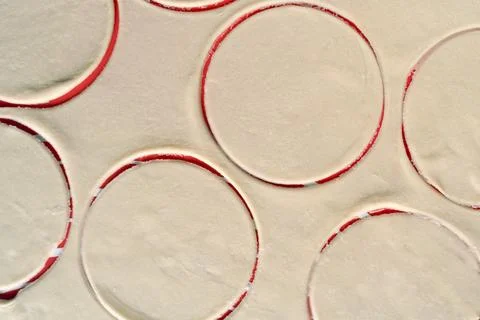 A close up of a sheet of dough with red circles cut out of it Stock Photos