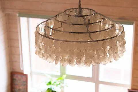 Close up of a shell chandelier hanging in front of a bright window inside a warm Stock Photos