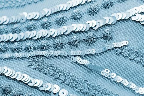 Close-up of shimmering silver sequins stitched on blue mesh fabric with tex.. Stock Photos