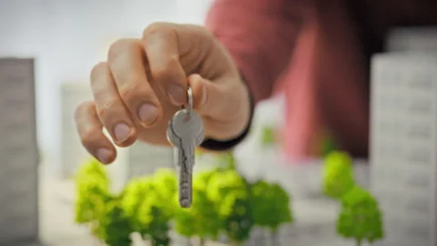 A close-up of shiny keys held out by a mans hand against a backdrop of minia Stock Footage 344877040