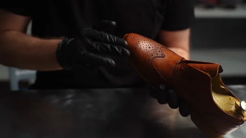 Close-up of shoemaker in black gloves rubbing paint on toe cup of brown leather Video stock 150012598
