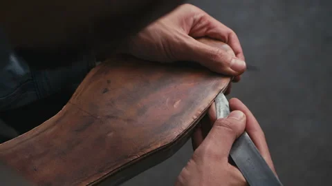 Close-up shoemaker cuts knife through leather sole at production shoes Stock Footage 138307333
