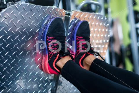 Close up shoes on platform. Fit woman working out leg press machine in gym Stock Photos