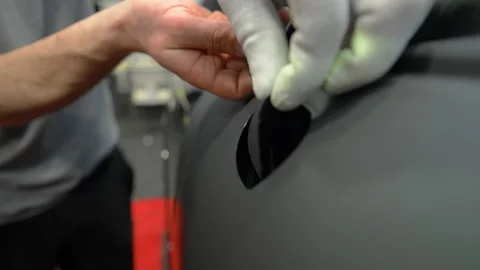 Close up shoot of a cutting vinyl wrap on a car body panel in a workshop Stock Footage 334056226