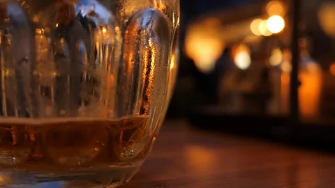 Close up shoot of a pint of a cold beer on a pub table, golden evening, people s Stock Footage 116529213