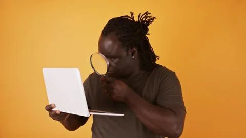 Close up shot of an african man using magnifying glass to read from laptop Stock Photos