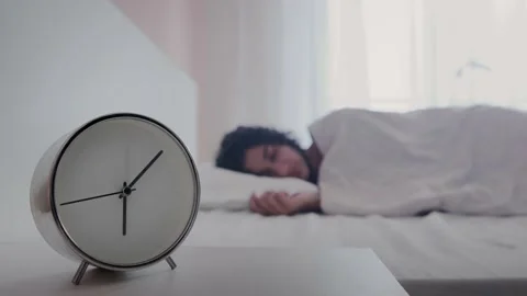 Close up shot of alarm clock on table with young woman sleeping comfortably Video stock 230303595