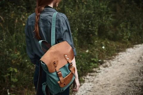 Close shot of the back of a red-haired girl with a backpack standing on the road Stock Photos