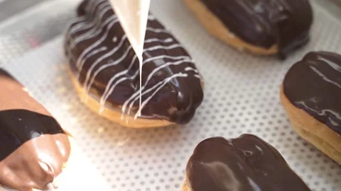 Close-up shot of a baker glazing the eclairs with white chocolate at the bakery Stock Footage 164401660