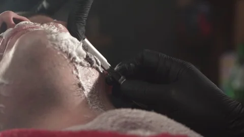 Close up shot of barber in black gloves cut beard of client with straight razor Stock Footage 125055464