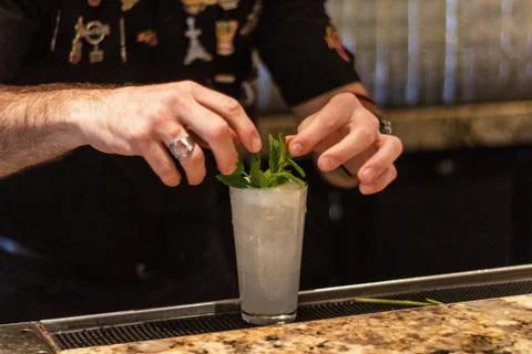 A close shot of a bartender putting a mint leaf on a cocktail with a blurred  Stock Photos