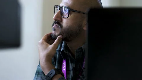 A close up shot from behind an office desk as an Asian man sits gazing out Stock Footage 201183435