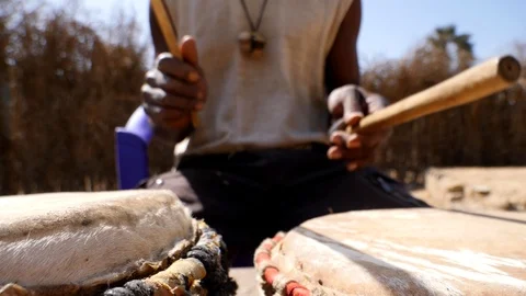 Close shot of black man playing dundun with wooden sticks while sitting Video stock 113166360