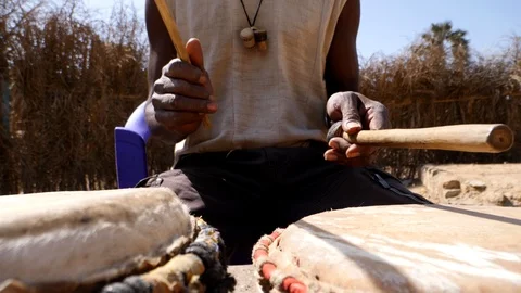 Close shot of black man playing dundun with wooden sticks while sitting Video stock 113166474