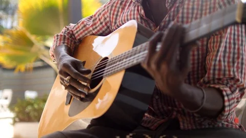 Close shot of black man playing acoustic guitar sitting on chair Stock Footage 116232415