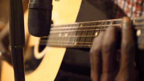 Close shot of black man playing acoustic guitar sitting on chair in recording Video stock 116273825
