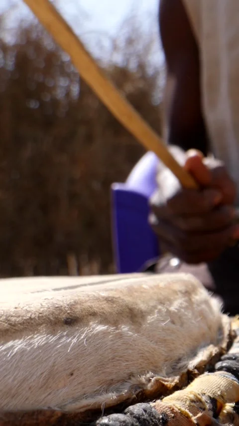 Close shot of black man playing dundun with wooden sticks while sitting Video stock 230663758