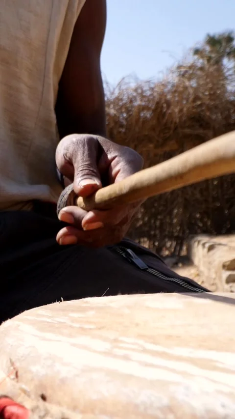 Close shot of black man playing dundun with wooden sticks while sitting Stock Footage 230663830