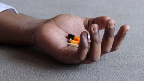 Close shot of a black man's hand lying dead on the floor, filled with medicines Stock Footage 147110689