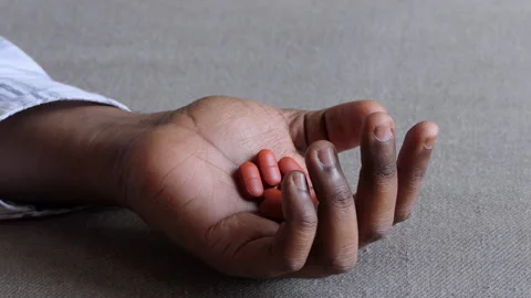 Close shot of a black man's hand lying on the floor and palm filled with tablets Stock Footage 147112495