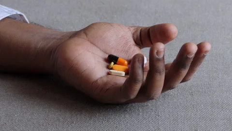 Close shot of a black man's hand lying on the floor, palm filled with medicines Stock Footage 147112497