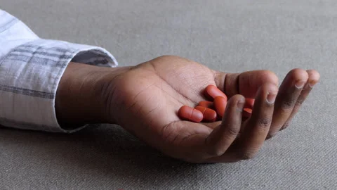 Close shot of a black man's hand lying on the floor and tablets fall on his hand Stock Footage 147113334