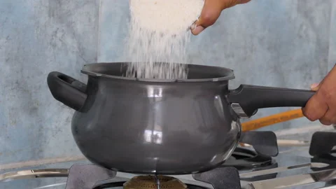 Close shot of a black pressure cooker, hand pouring rice in it Stock Footage 147251663