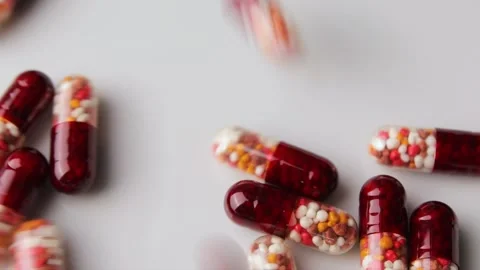 Close up shot of capsules with multi-colored granules fall on a white surface Stock Footage 274503143