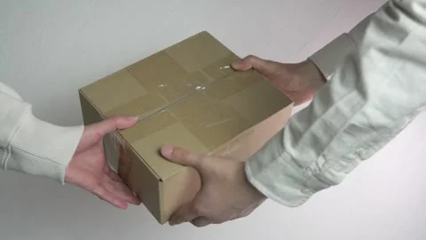 A close-up shot captures a box being carefully passed from a mans hands to a 스톡 동영상 318580865