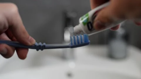 Close-up shot of caucasian hands squeezing toothpaste onto a blue brush in Stock Footage 204720865