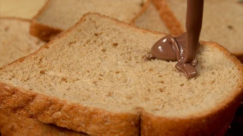 Close up shot of choco spread falling on a brown bread in a beautiful pattern Stock Footage 113335076