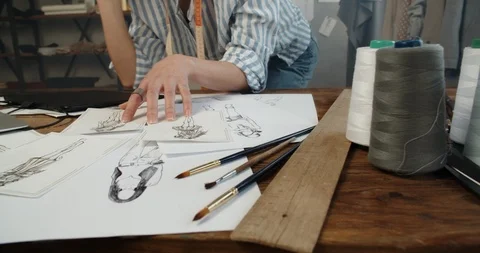 Close-up shot of a clothes designer redrawing beautiful sketches from paper to Stock Footage 124612669