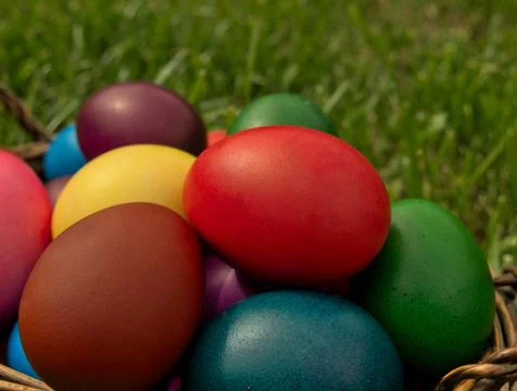 A close up shot of colorful Easter eggs in a wicker basket stand on the grass Stock Photos