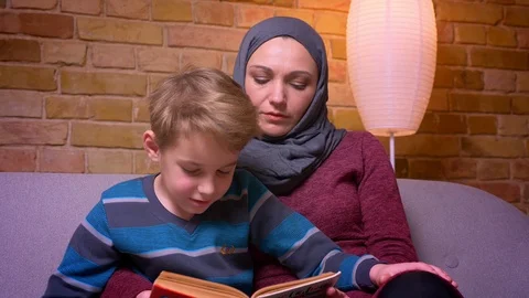 Close-up shot of concentrated small boy and his muslim mother in hijab reading Stock Footage 108115128